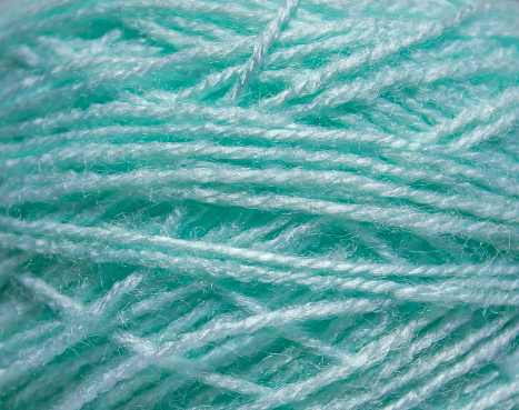 Macro texture of woolen turquoise thread, close-up, copy space. Macro Photography of a coil with threads. Sewing background, screensaver. Abstraction, interweaving of natural threads