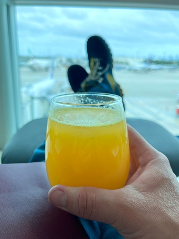 POV Personal perspective view to the airport runway, while a latin young man is relaxing and drinking an orange juice in a VIP Lounge at the airport waiting for the boarding time at Miami International Airport, Florida, USA.