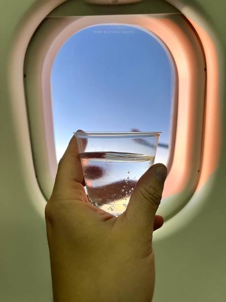 istock POV Personal perspective view to porthole  while a latin young man is relaxing and drinking a cup with sparkling water inside an airplane sitting in economy class during the fly. 1968236687