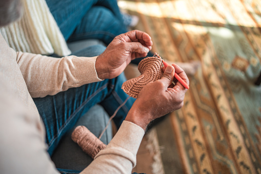 Close-up of elderly individual's hands while knitting with brown yarn, showcasing traditional craftsmanship and hobby activities.