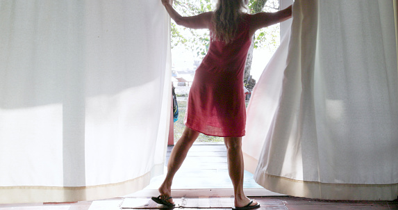 Mature woman opens curtains in morning and walks through glass doorway