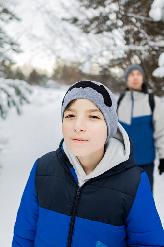 Father and son are hiking through forest on a snowy winter day. Happy family weekend. Portrait of a boy in warm winter clothing.
