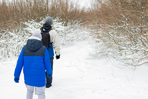 Father and son are hiking through forest on a snowy winter day. Happy family weekend.