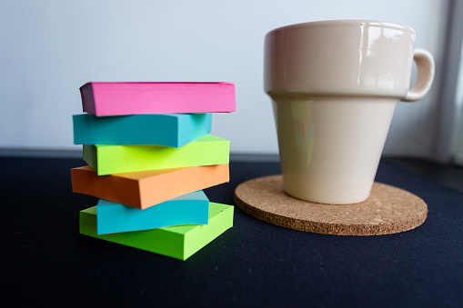 Stack of colorful sticky notes beside a coffee cup on a desk.