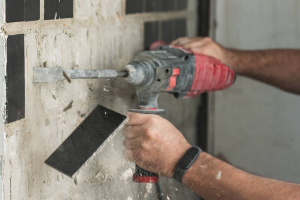 istock Builder with a puncher dismantles old tiles from a concrete wall 1968353136