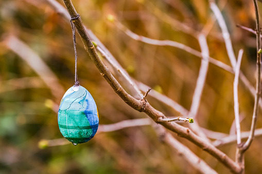 An egg for Easter hangs forgotten on a branch on a barren bush in winter