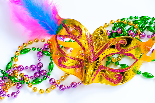 Golden carnival mask and colorful beads on white background. Closeup symbol of Mardi Gras or Fat Tuesday. Holiday decorations in gold, green and purple.