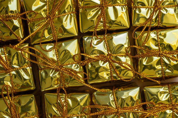Close up of a gift wrapped in pinstripe green paper with golden ribbon and confetti.