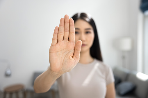 Serious Asian woman showing hand stop gesture, symbol of forbidding, danger, rejection, restriction. Close up of open palm with female model in blurred background