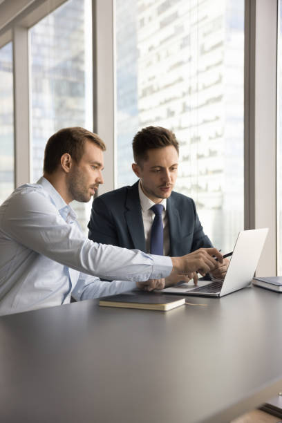 istock Two serious businessmen working at laptop, sitting at workplace table 1968420332