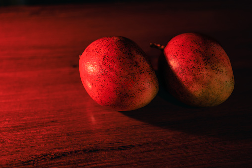 Two ripe tropical fruit on a shiny rosewood table. The colour of the mangoes indicate they are ready to eat.