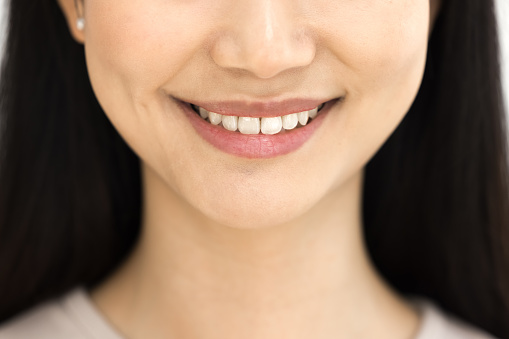 Toothy smile of happy young Asian woman showing healthy white teeth. Dental patient girl promoting dentist service, enamel bleaching, whitening, tooth paste. Cropped close up shot of lower face