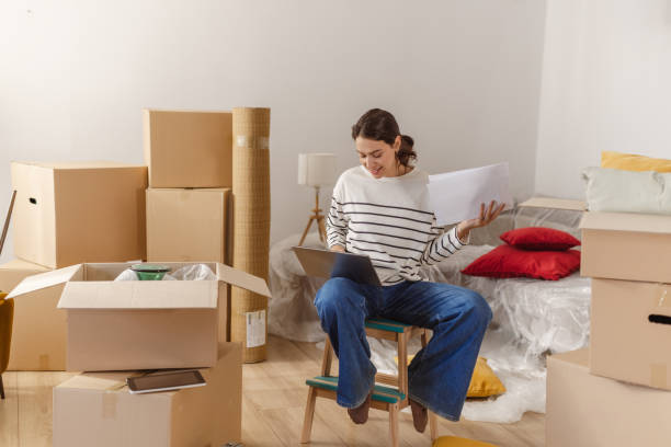 istock Young woman using laptop in new home and holding documents 1968464410