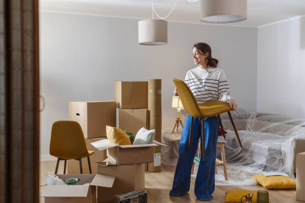 Smiling young woman surrounded by boxes while moving, unpacking personal belongings