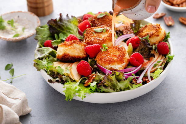 Fried goat cheese salad with apples and raspberries and vinaigrette dressing Fried goat cheese salad with apples and raspberries and berry vinaigrette dressing pouring over, action shot spring mix lettuce leaves stock pictures, royalty-free photos & images