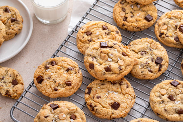 chocolate chip cookies on a cooling rack with flaky salt served with milk - chocolate chip cookie cookie chocolate stack photos et images de collection