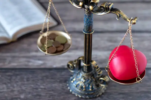 Photo of Balance scales with red heart shape and coins with holy bible book in the background