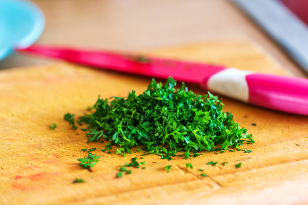 A close-up view of freshly cropped parsley arranged on a rustic wooden board, with a sharp knife poised nearby.