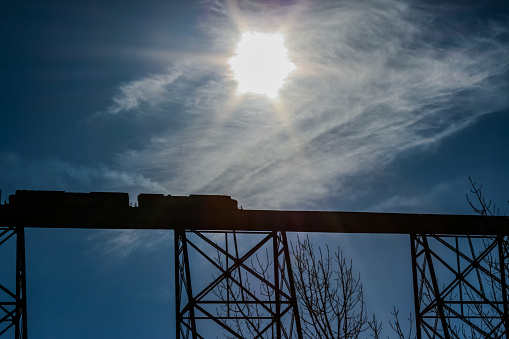 Smoke is seen coming from two Canadian Pacific Railroad train engines facing away from each other.  They are silhouetted going across the High Level Bridge/Lethbridge Viaduct in Lethbridge, Alberta, Canada.  It is the highest and longest combined trestle bridge in the world.  It runs between coulee edges over the Oldman River.