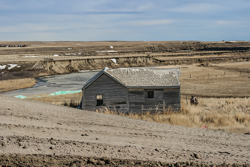 An old wood house beside the Milk River in Southern Alberta, Canada.  Built in the early 1900’s and abandoned for decades, there is extensive wear showing  This house was built for settlers who moved up from the United States.  It was torn down in 2008 to make room for an expanded highway, construction of which is seen in this photo.  A photo has also been submitted that shows a close up of the front left window, looking through the building.