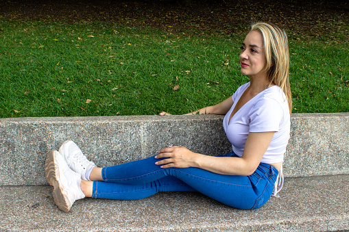 Beautiful young woman sitting on a concrete bench with her legs stretched