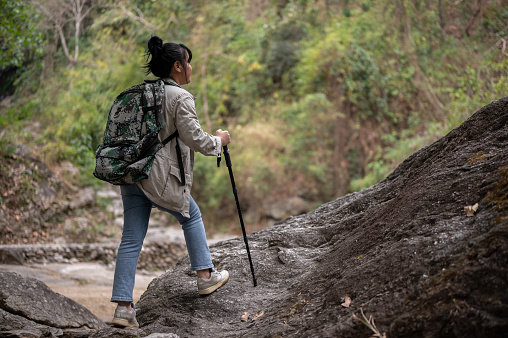 Back view of an adventure Asian woman with a backpack and a trekking pole is hiking on a rock mountain alone. fun activity, travel, explorer