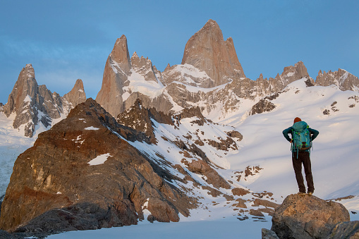 Backpacker stands on rock below mountain range in twilight