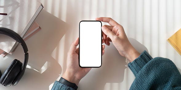 Top view mockup image of a woman holding mobile phone with blank white screen while sitting.