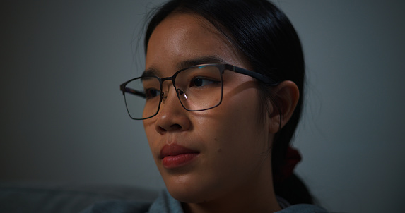 Selective focus ,Face of Young woman wearing glasses sitting on sofa thinking of problems while sitting alone on the sofa in living room at home,looking thoughtful.depression