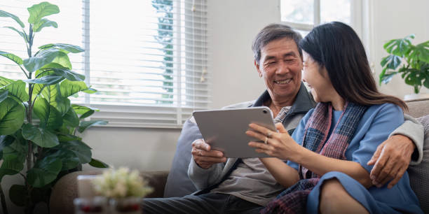 istock Happy elderly asian couple using tablet sit on sofa doing ecommerce shopping online on website and buying insurance browsing at home 1968880986
