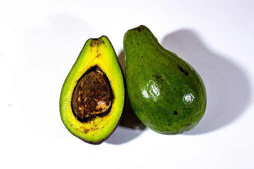 one whole green avocado and a slice of avocado with bright yellow flesh, on a plain white background