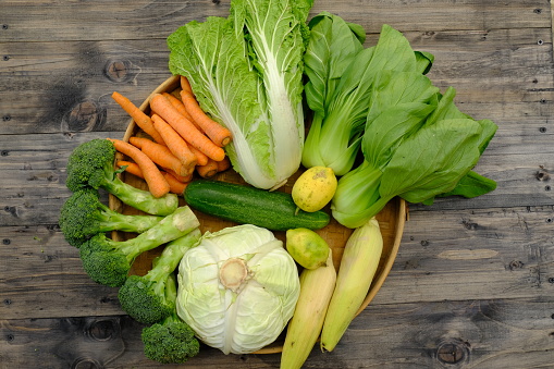 assorted vegetables on bamboo woven container. broccoli, mustard, carrot, cabbage, pak choi, sweet corn, lemon, cucumber.