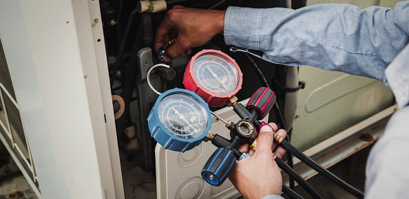 Air conditioner technician is using a manifold gauge to check the refrigerant in the system to inspect and repair the outdoor air compressor.