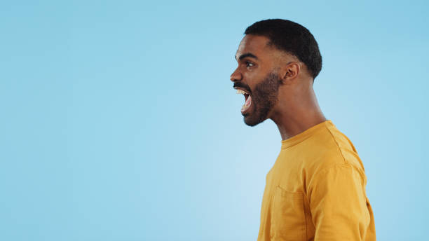 stress, angry and man shouting in studio with anxiety, frustrated or disaster on blue background. mistake, fail and profile of guy model with screaming reaction to mental health crisis, fear or panic - aggression control clothing image type imagens e fotografias de stock