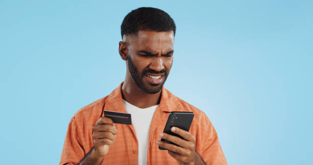 istock Man, credit card and confused with phone, studio and thinking of price, code or info by blue background. Online shopping, payment glitch or mistake with declined account with fintech with smartphone 1969010598