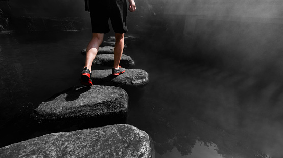 Man walking crossing river on stones bridge