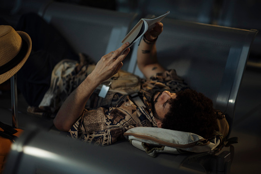 A young man reading a book on the airport bench