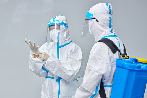 Two healthcare worker wearing to protective workwear at gray backgrounds.