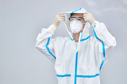 One male healthcare worker wearing to protective workwear at gray backgrounds.