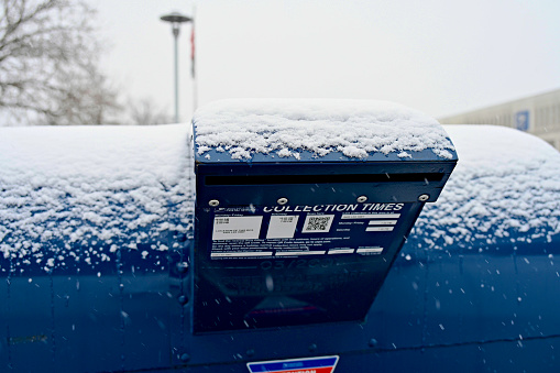 Merrifield, Virginia, USA - January 15, 2024: Freshly fallen snow covers the top of a large mail deposit box at the U.S. Postal Service’s Merrifield processing center during the first significant winter storm of the year in the Northern Virginia area.