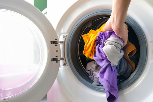 A woman opens the front door of a washing machine and puts clothes into the washing machine to clean and disinfect. Clean and healthy concept