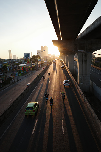 Bangkok, Thailand - November 24, 2023: Silhouetted scene of morning transportation on main road under sky train railway in Bangkok, Thailand with golden sunlight.