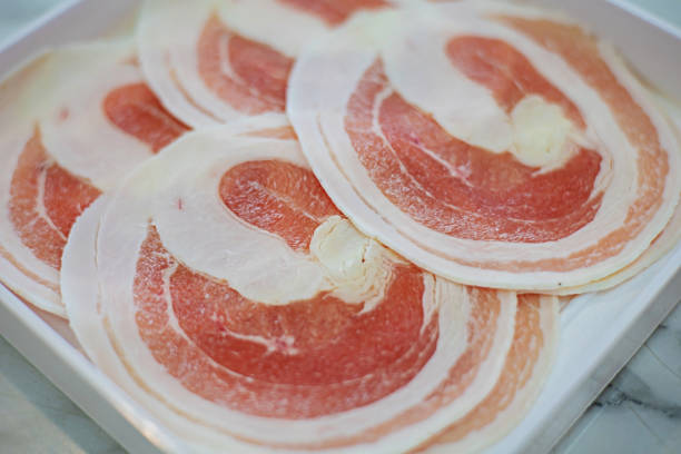 Thinly sliced pork belly is placed in a white plate on a marble patio table at Shabu Shabu.