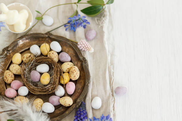 istock Happy Easter! Colorful easter chocolate eggs in nest, spring flowers, feathers and linen cloth on rustic wooden table. Space for text. Easter modern simple decoration 1969168644