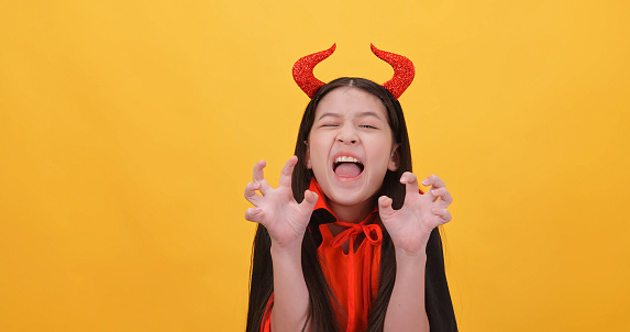 Cute little girl wearing a witch costume to celebrate Halloween on yellow background.