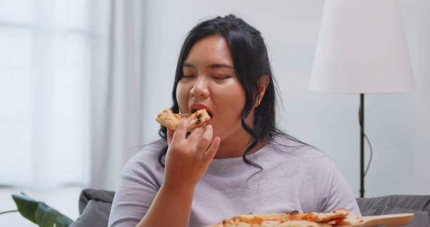 istock A chubby Asian woman enjoying pizza while relaxing on the sofa at home. 1969206949