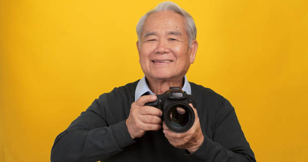 istock Old Asian man taking photo with digital camera, isolated on yellow background in the studio. 1969207515