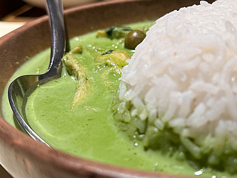 Stock photo showing close-up view of bowl of spicy Thai Green Curry with chicken recipe made with coconut milk or coconut cream, chicken broth, chicken, peas, fish sauce, sugar, Kaffir lime leaves, Thai green curry paste and red chilli garnish.