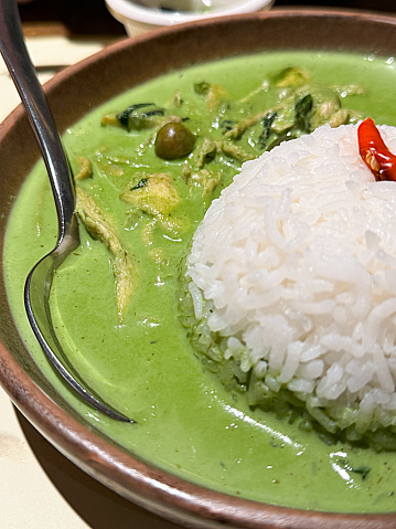 Stock photo showing close-up view of bowl of spicy Thai Green Curry with chicken recipe made with coconut milk or coconut cream, chicken broth, chicken, peas, fish sauce, sugar, Kaffir lime leaves, Thai green curry paste and red chilli garnish.