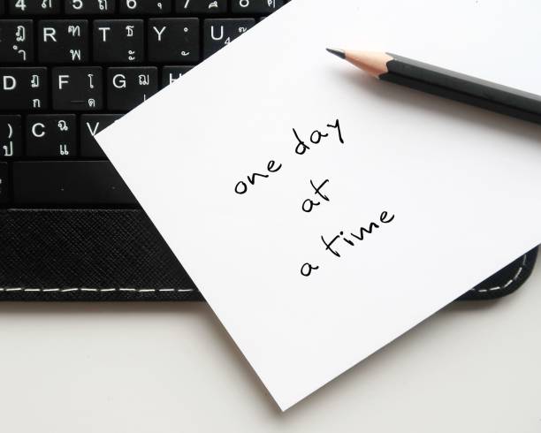 Paper on keyboard with handwritten text ONE DAY A TIME, concept of dealing with each day problems as they come, less worry about future or expect things to change overnight